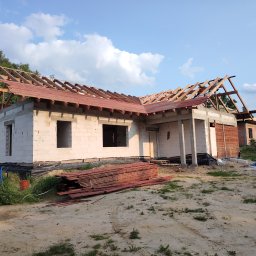 Radek Ambroziak - Budowa domu jednorodzinnego w trakcie realizacji: ściany z betonu komórkowego, częściowo wykonana więźba dachowa z deskowaniem, widoczne materiały budowlane.