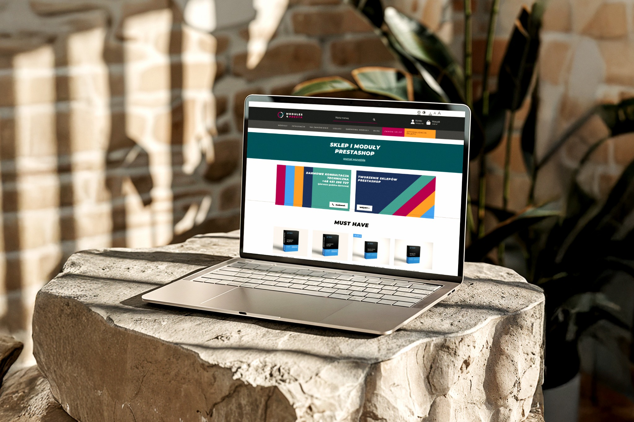 Laptop z otwartą stroną sklepu internetowego na kamiennym blacie, w tle ceglana ściana i roślina. Prezentacja modułów PrestaShop na tle naturalnych materiałów.