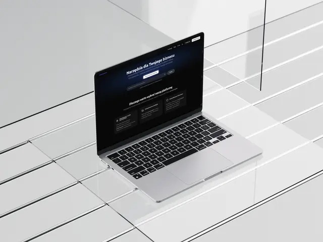 Laptop z otwartą stroną internetową na błyszczącym, białym tle. Minimalistyczny design, ciemny interfejs strony kontrastuje z jasnym otoczeniem. Widok z góry, czysty kadr.