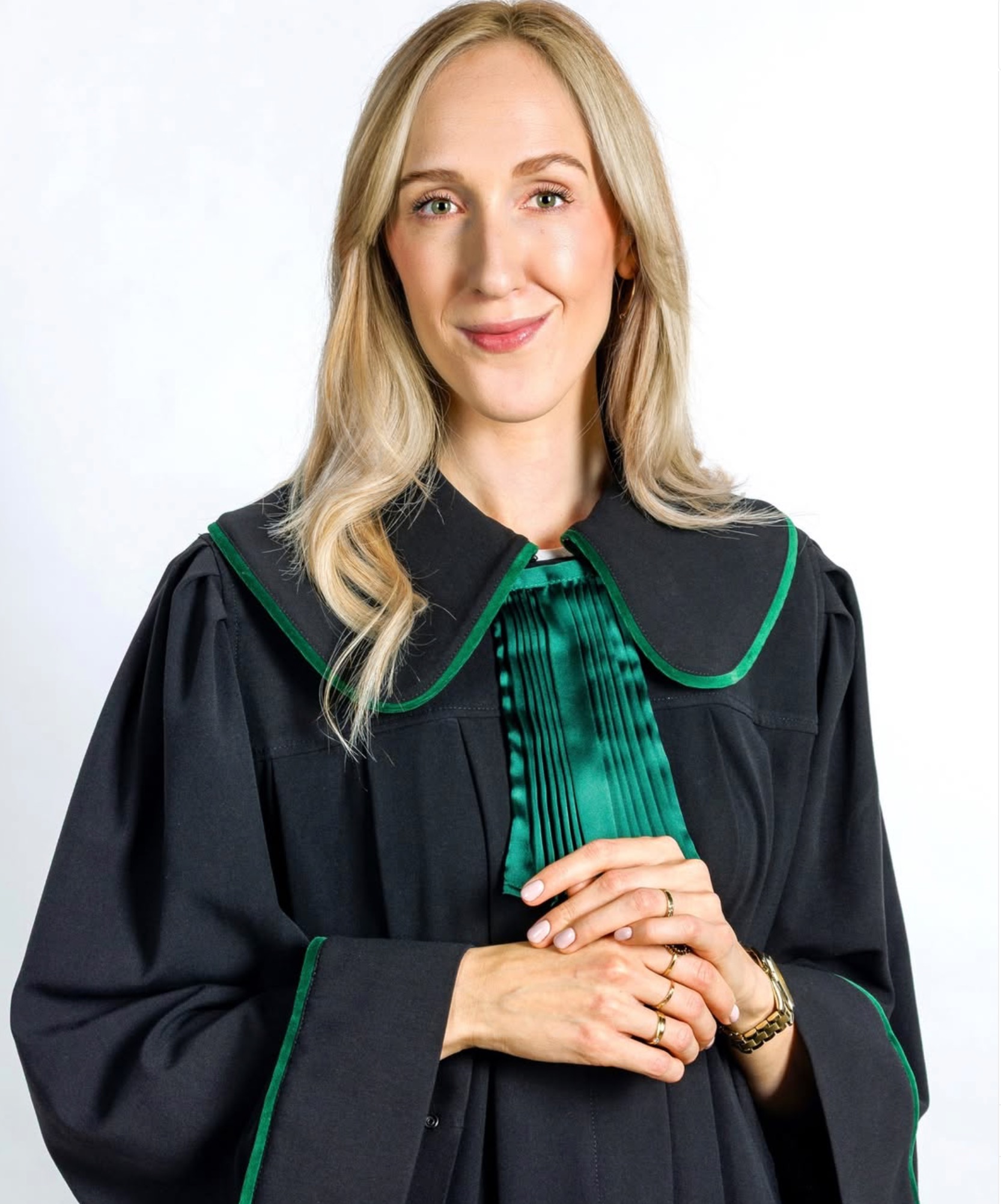 Portret uśmiechniętej kobiety w todze adwokackiej z zielonymi akcentami, na jasnym tle. Widoczne dłonie z pierścionkami i zegarek.