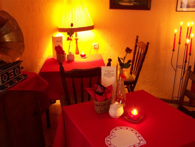 Ustawione stoliki w herbaciarni z czerwonymi obrusami, świecami, gramofonem i lampą ze zdobieniami, tworzące romantyczny nastrój.
