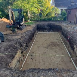 Marcin Bieniek Ogrody-Bieniek - Wykop pod fundamenty z wytyczonym obrysem, widoczny sprzęt budowlany: minikoparka i ładowarka. Na drugim planie budynek mieszkalny i drzewa.