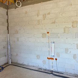 Elektryk - Surowy mur z instalacją elektryczną: pomarańczowe puszki, kable w peszlach, rury. Widoczne przygotowania do rozprowadzenia instalacji w nowym budynku.