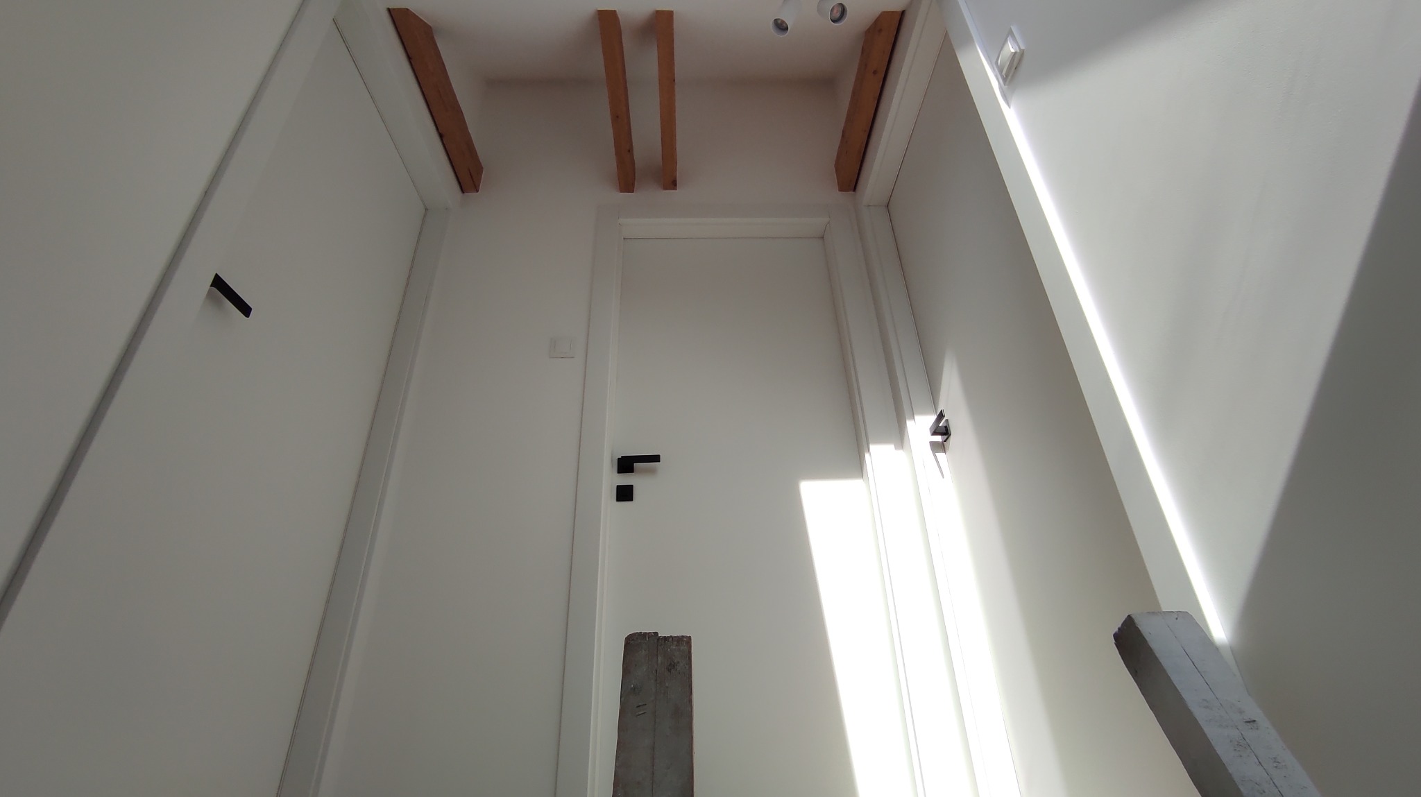 Białe wnętrze z zamontowanymi drzwiami i drewnianymi elementami konstrukcyjnymi pod sufitem, uchwycone z perspektywy żabiej.