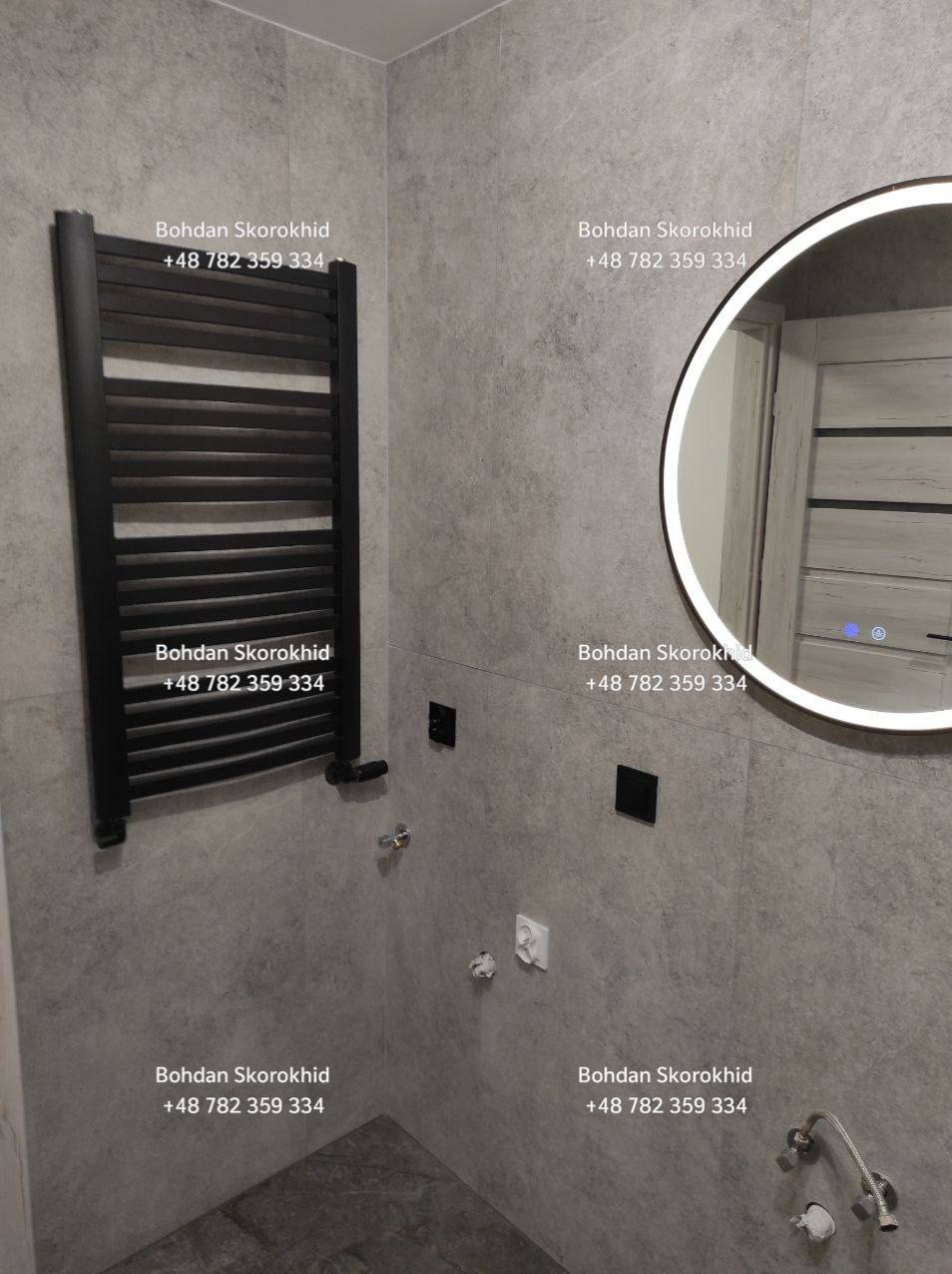 Wykończona łazienka w Szczawnie-Zdroju: szare płytki, czarny grzejnik drabinkowy, okrągłe lustro z podświetleniem LED i minimalistyczna armatura.