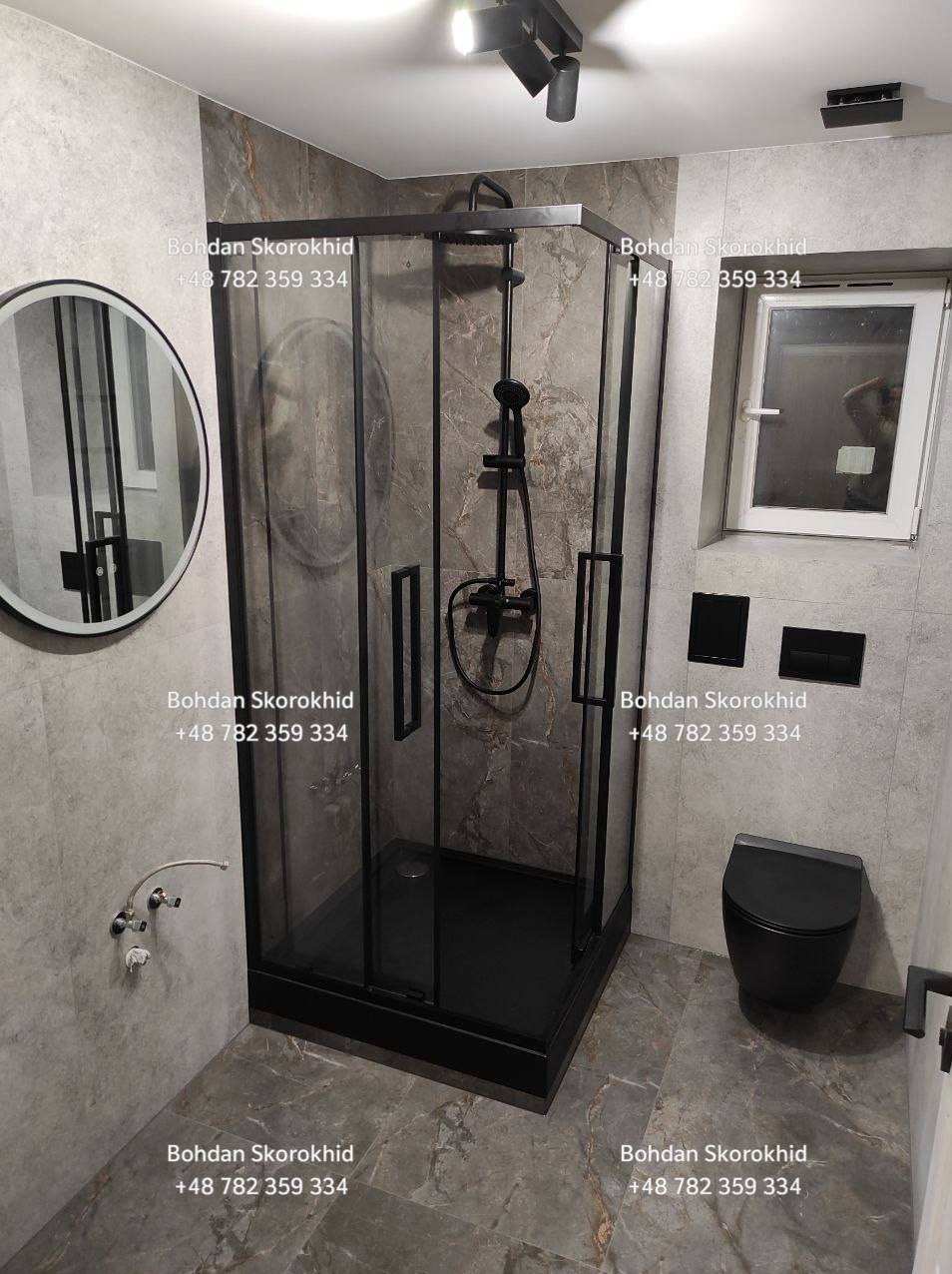 Nowoczesna łazienka z kabiną prysznicową w czarnej ramie, okrągłym lustrem i szarą marmurową płytką. Minimalistyczny design, czarna armatura i oświetlenie punktowe.