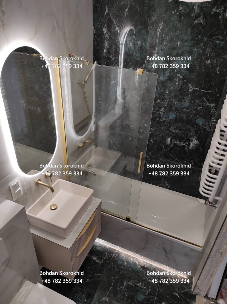 Elegancka łazienka z marmurowymi płytkami, podświetlanym lustrem i złotymi akcentami. Umywalka nablatowa na szafce z frezowanymi frontami. Kabina nawannowa ze złotymi okuciami.