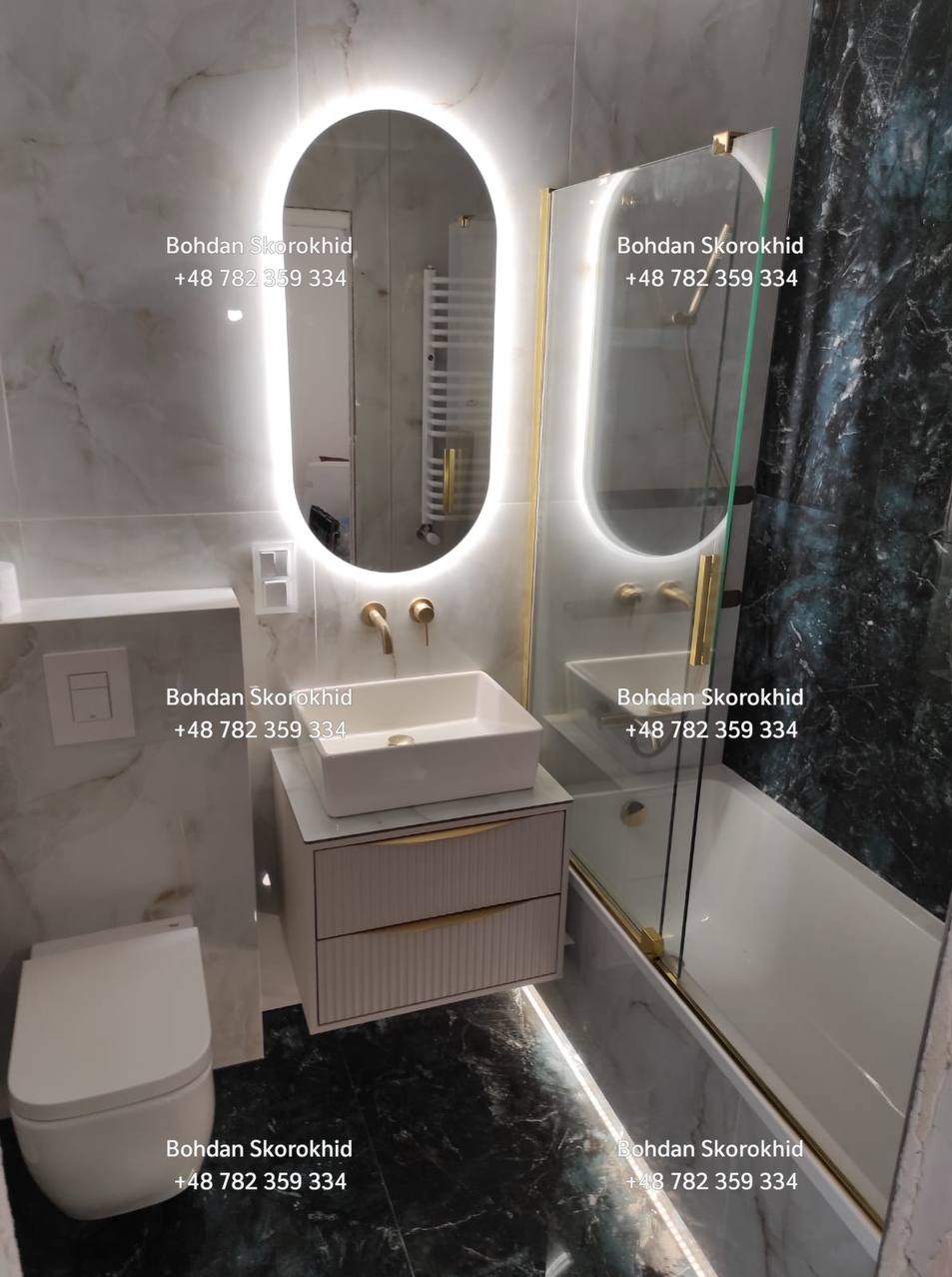 Nowoczesna łazienka z owalnym lustrem LED, białą umywalką na szafce z frezowanymi frontami i kabiną prysznicową ze złotymi detalami na tle marmurowych płytek.