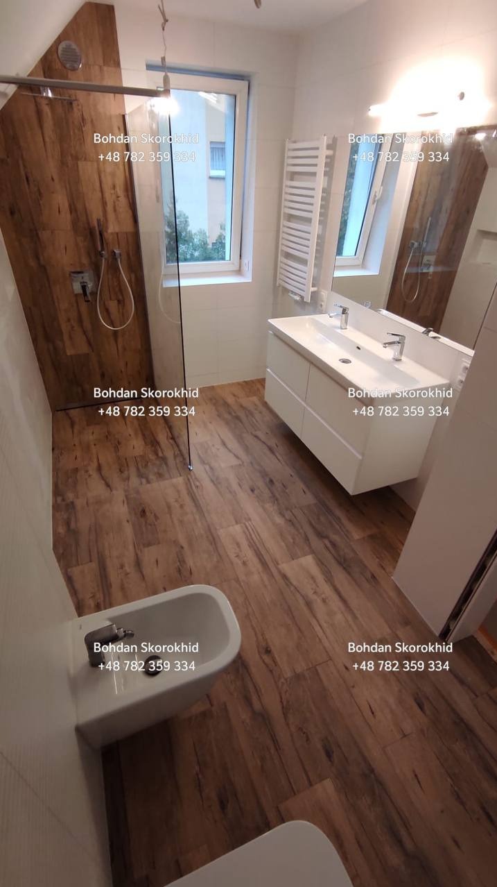 Nowoczesna łazienka z drewnopodobną podłogą i ścianą prysznicową, białą armaturą i szafką umywalkową. Minimalistyczny design z akcentem naturalnego drewna.