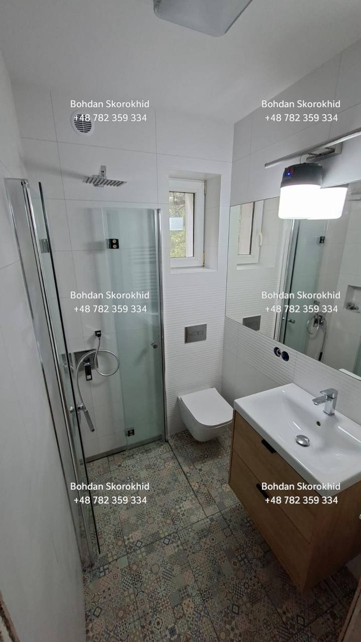 Nowoczesna łazienka po remoncie: kabina prysznicowa ze szklanymi drzwiami, umywalka z szafką z jasnego drewna i toaleta w minimalistycznym stylu. Na podłodze wzorzyste płytki.