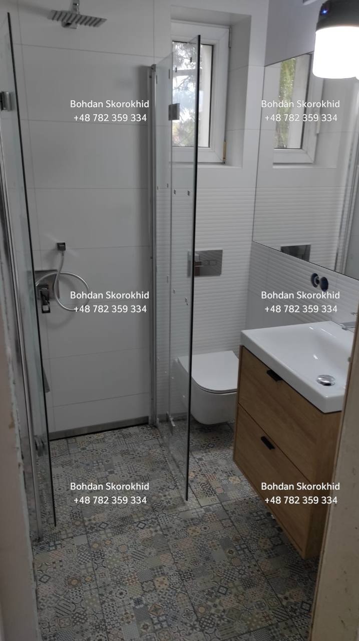 Nowoczesna łazienka po remoncie: kabina prysznicowa ze szklanymi drzwiami, umywalka z szafką z jasnego drewna i wzorzysta podłoga. Minimalistyczny design, białe płytki.