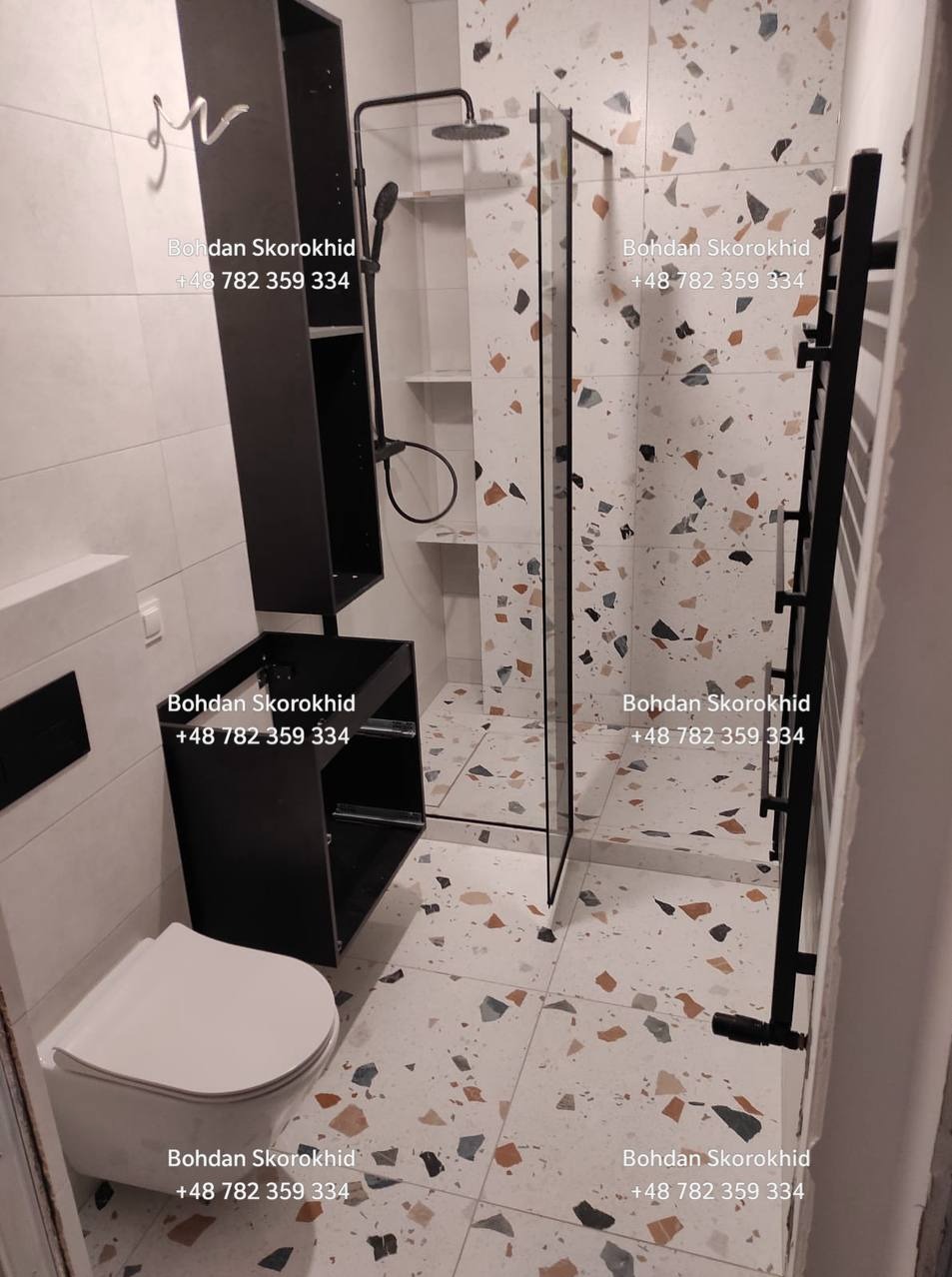 Wykończona łazienka z kabiną prysznicową typu walk-in, wiszącą toaletą i czarnymi meblami łazienkowymi na tle płytek lastryko. Nowoczesny design.