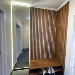 Perfect Wnętrza - Nowoczesna aranżacja przedpokoju: drewniana boazeria z siedziskiem, lustro z podświetleniem LED, marmurowa podłoga. Minimalistyczny design, ciepłe oświetlenie.