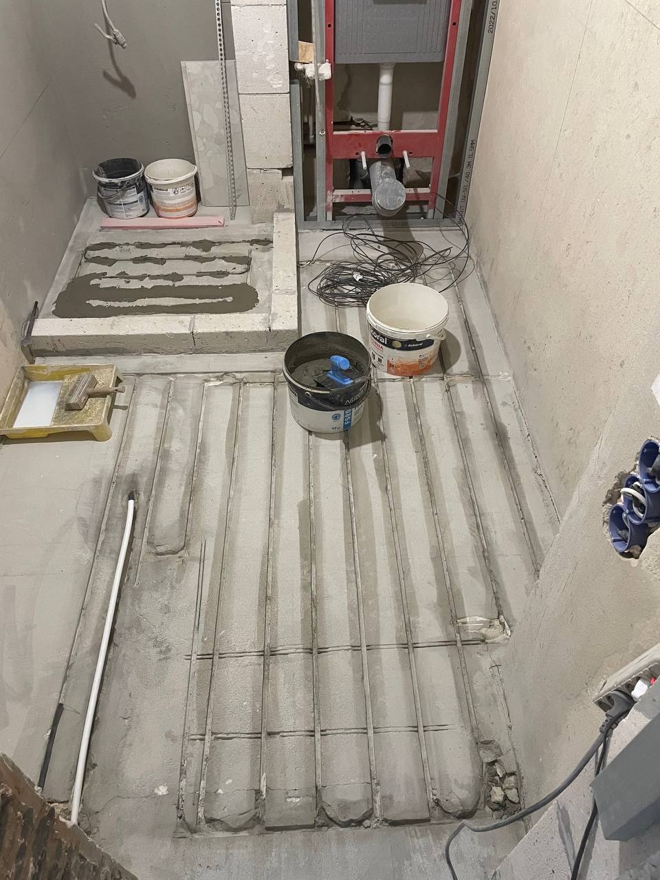 Montaż ogrzewania podłogowego w łazience, widoczne rury grzewcze zatopione w wylewce, przygotowane do dalszych prac wykończeniowych.