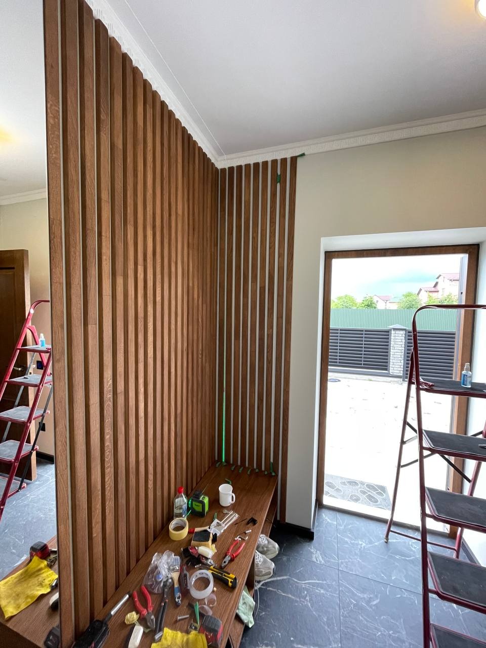 Montaż drewnianej ścianki działowej z pionowych listew w jasnym wnętrzu. Widoczne narzędzia i drabina, sugerujące etap prac wykończeniowych.