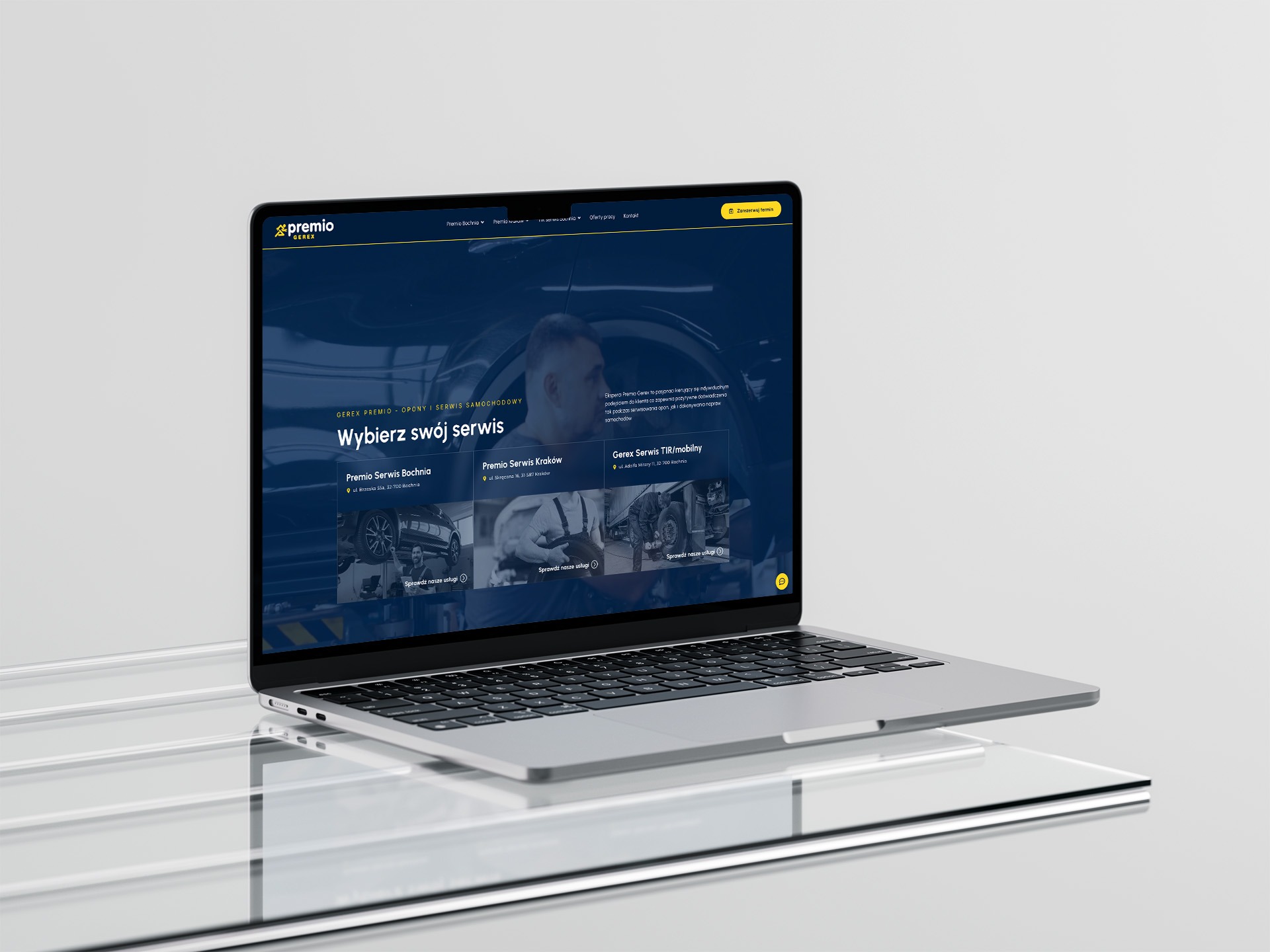 Laptop wyświetla stronę internetową Premio, prezentującą ofertę serwisów samochodowych. Strona z ciemnym tłem i żółtymi akcentami, z widocznymi adresami serwisów.
