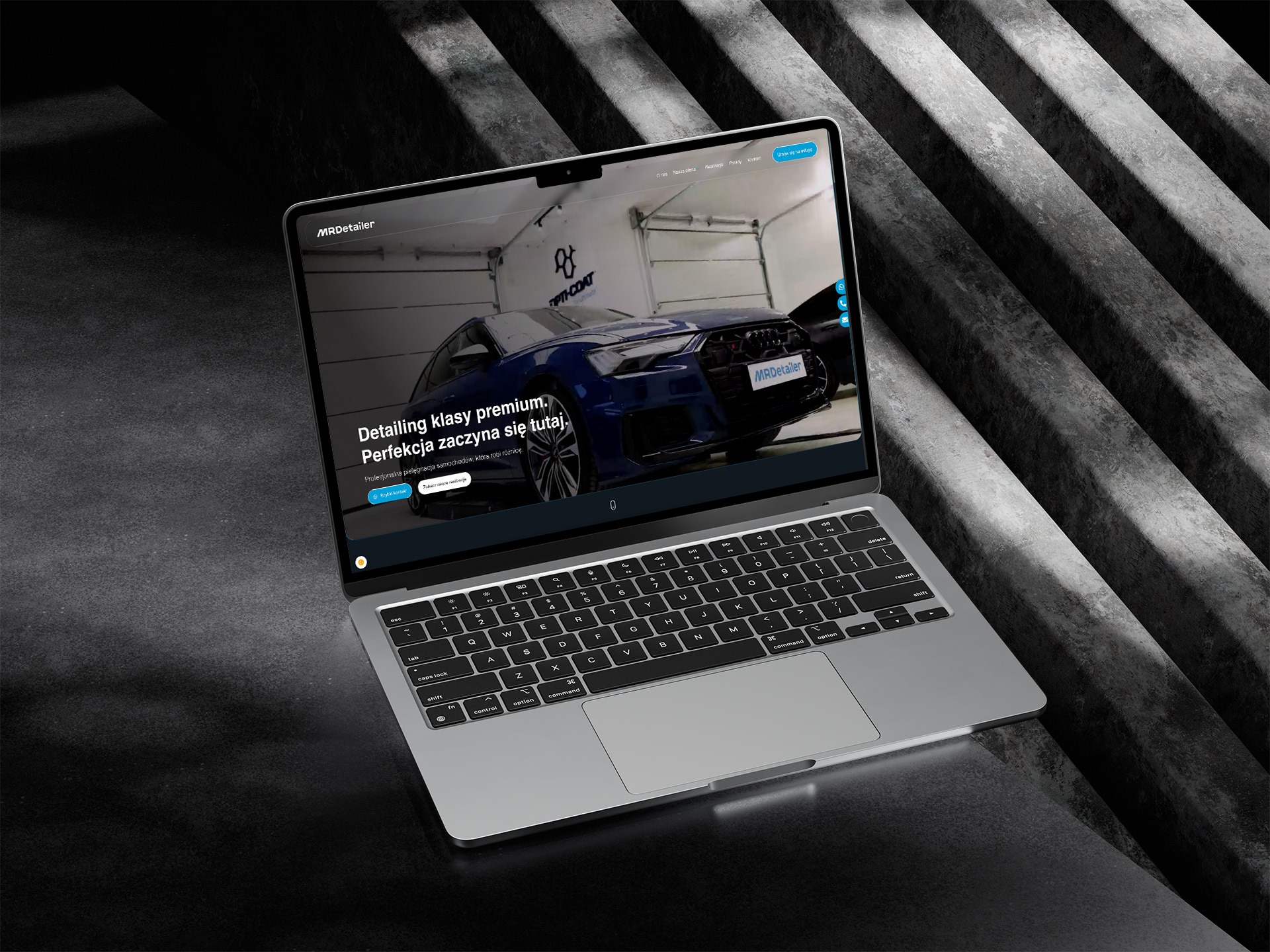 Laptop wyświetla stronę MRDetailer z niebieskim Audi. Detailing klasy premium. Profesjonalna pielęgnacja samochodów. Nowoczesny design, ciemne tło, betonowe schody.