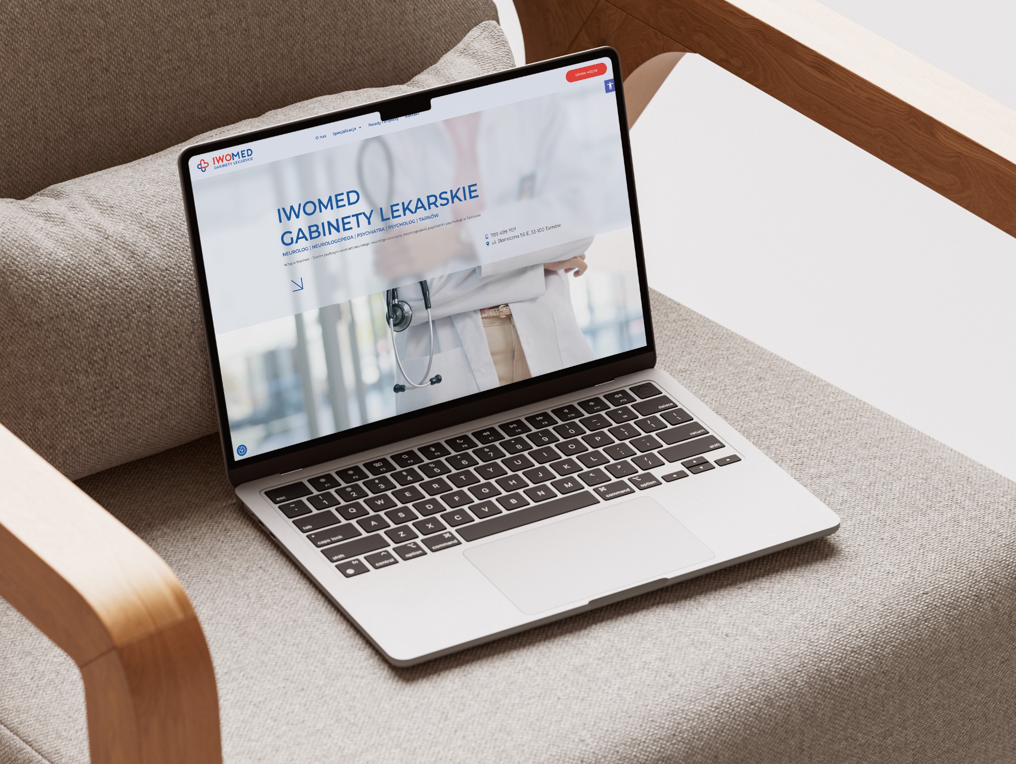 Laptop na fotelu prezentuje stronę internetową gabinetów lekarskich Iwomed z widocznym menu, logo i danymi kontaktowymi. Ekran oświetlony, klawiatura w kadrze.