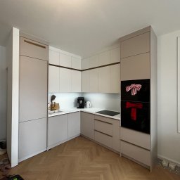 MODULove - Jasna kuchnia w kształcie litery L z beżowymi i białymi frontami, złotymi akcentami i parkietem w jodełkę. Na piekarniku świąteczne dekoracje.