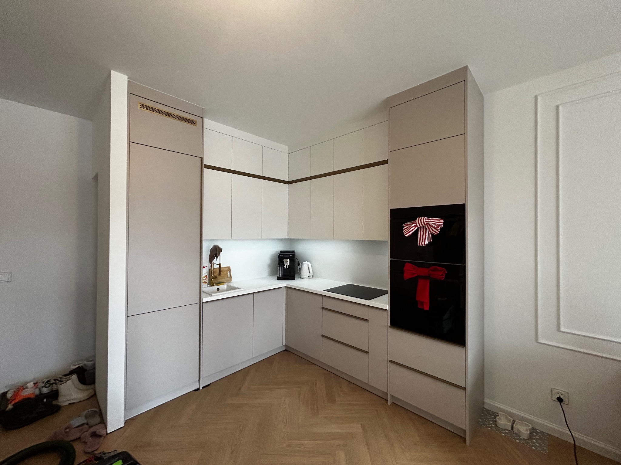 Jasna kuchnia w kształcie litery L z beżowymi i białymi frontami, złotymi akcentami i parkietem w jodełkę. Na piekarniku świąteczne dekoracje.