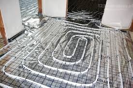 Białe rury ogrzewania podłogowego ułożone na czarnej siatce z folią aluminiową w tle, widok z góry, instalacja przed wylaniem posadzki.
