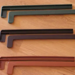 Trzy zestawy parapetów stalowych zewnętrznych w kolorach: zielonym, brązowym i ceglastym, leżące na drewnianej powierzchni.