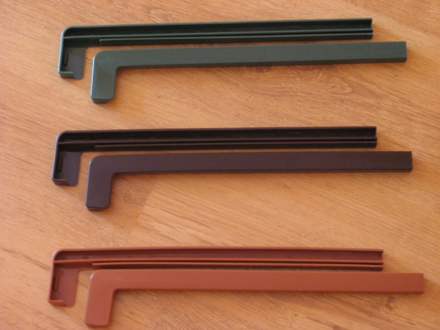 Trzy zestawy parapetów stalowych zewnętrznych w kolorach: zielonym, brązowym i ceglastym, leżące na drewnianej powierzchni.