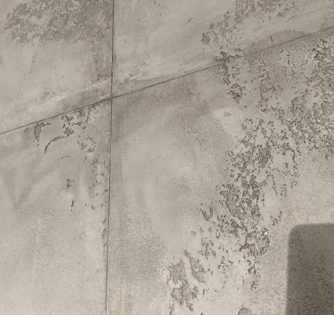 Szara ściana z efektem dekoracyjnym, imitującym beton lub tynk strukturalny, podzielona fugami na kwadraty. Widoczne nieregularne wzory i faktura.