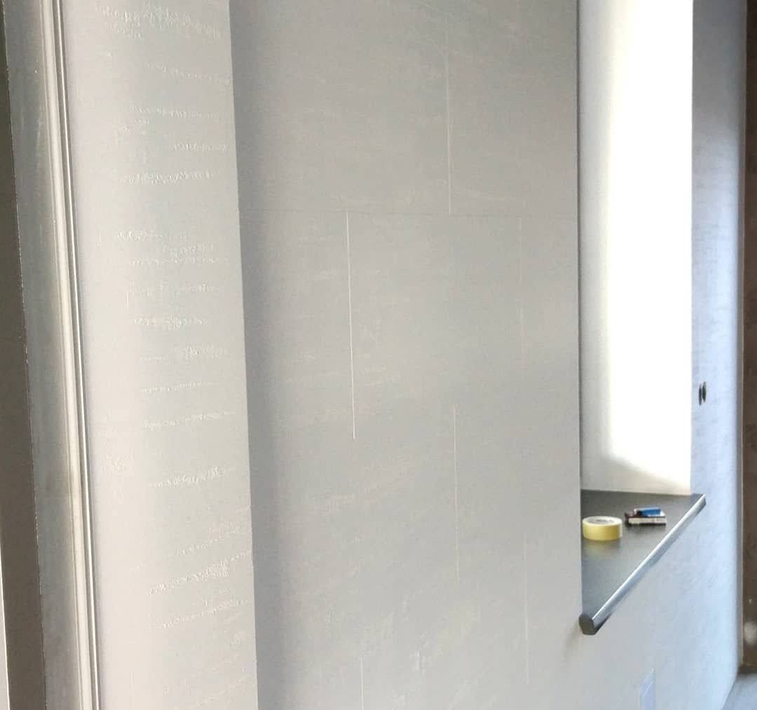 Ściana po malowaniu z efektem dekoracyjnym, widoczna taśma malarska na parapecie. Wykończenie wnętrza w odcieniach szarości, minimalistyczny styl.