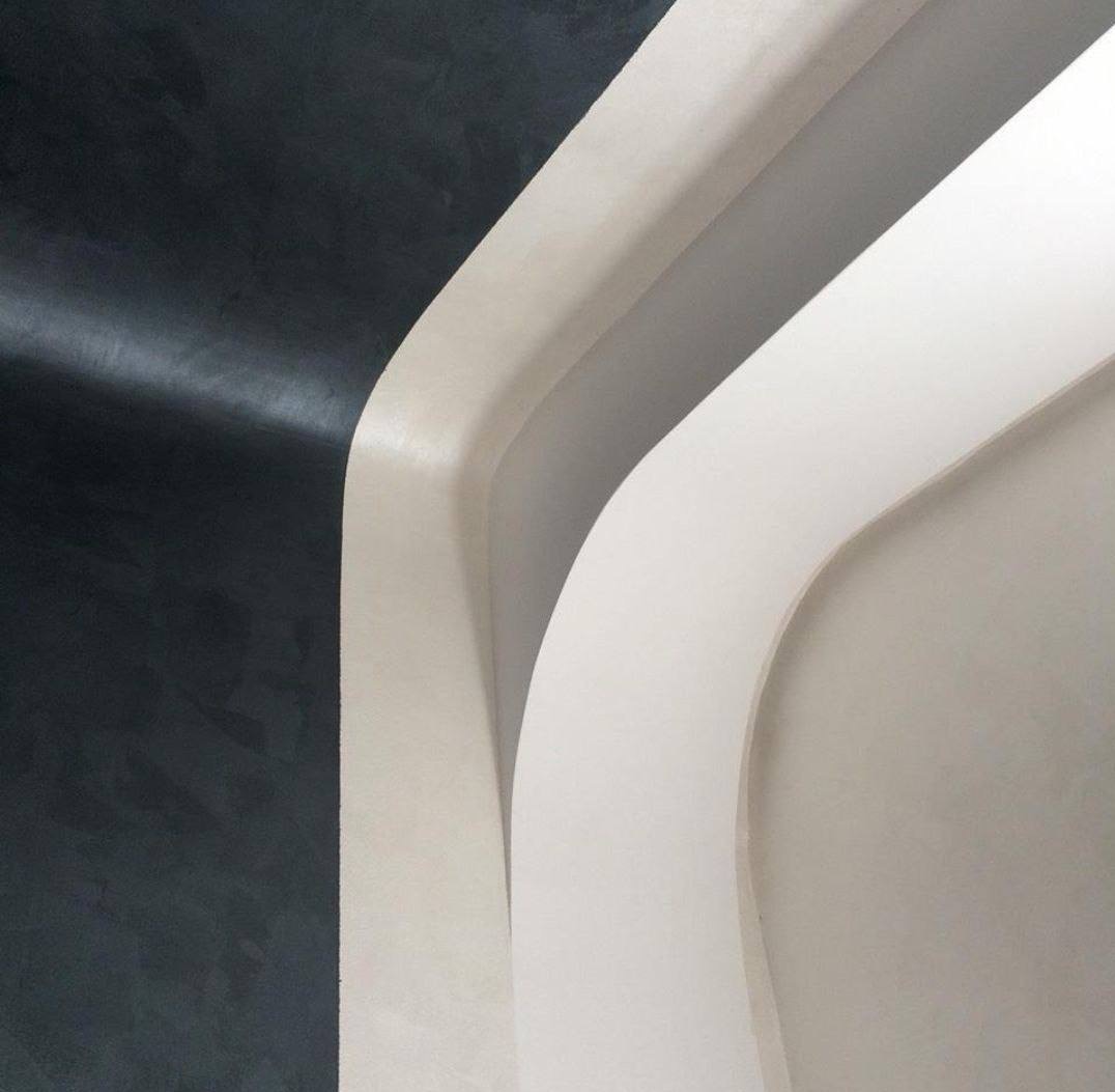 Minimalistyczne wykończenie wnętrza z ciemną, teksturowaną ścianą i zaokrąglonymi, jasnymi elementami architektonicznymi tworzącymi nowoczesny, abstrakcyjny wzór.