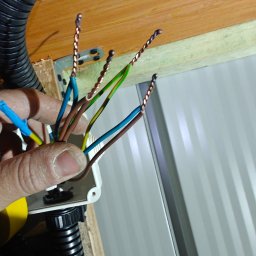 Dron Elektro - Podłączenie przewodów elektrycznych w puszce instalacyjnej, widoczne skręcone końcówki kabli i peszel. Praca w trakcie realizacji.