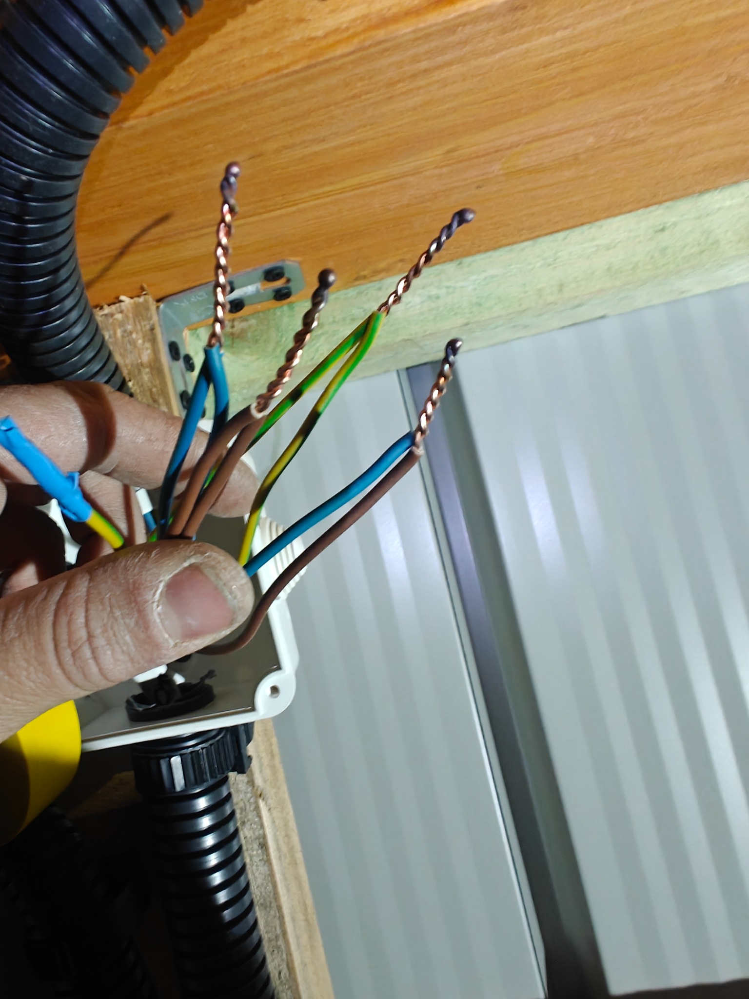 Podłączenie przewodów elektrycznych w puszce instalacyjnej, widoczne skręcone końcówki kabli i peszel. Praca w trakcie realizacji.