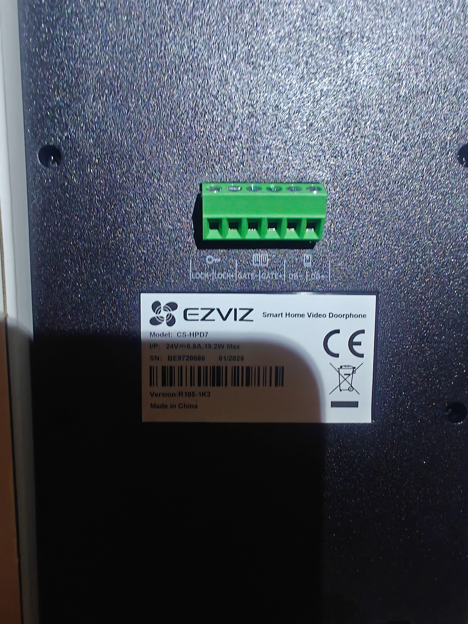 Tył wideodomofonu EZVIZ C5-HPD7 z zielonym złączem śrubowym i naklejką z danymi technicznymi, w tym numer seryjny i informacje o zasilaniu.