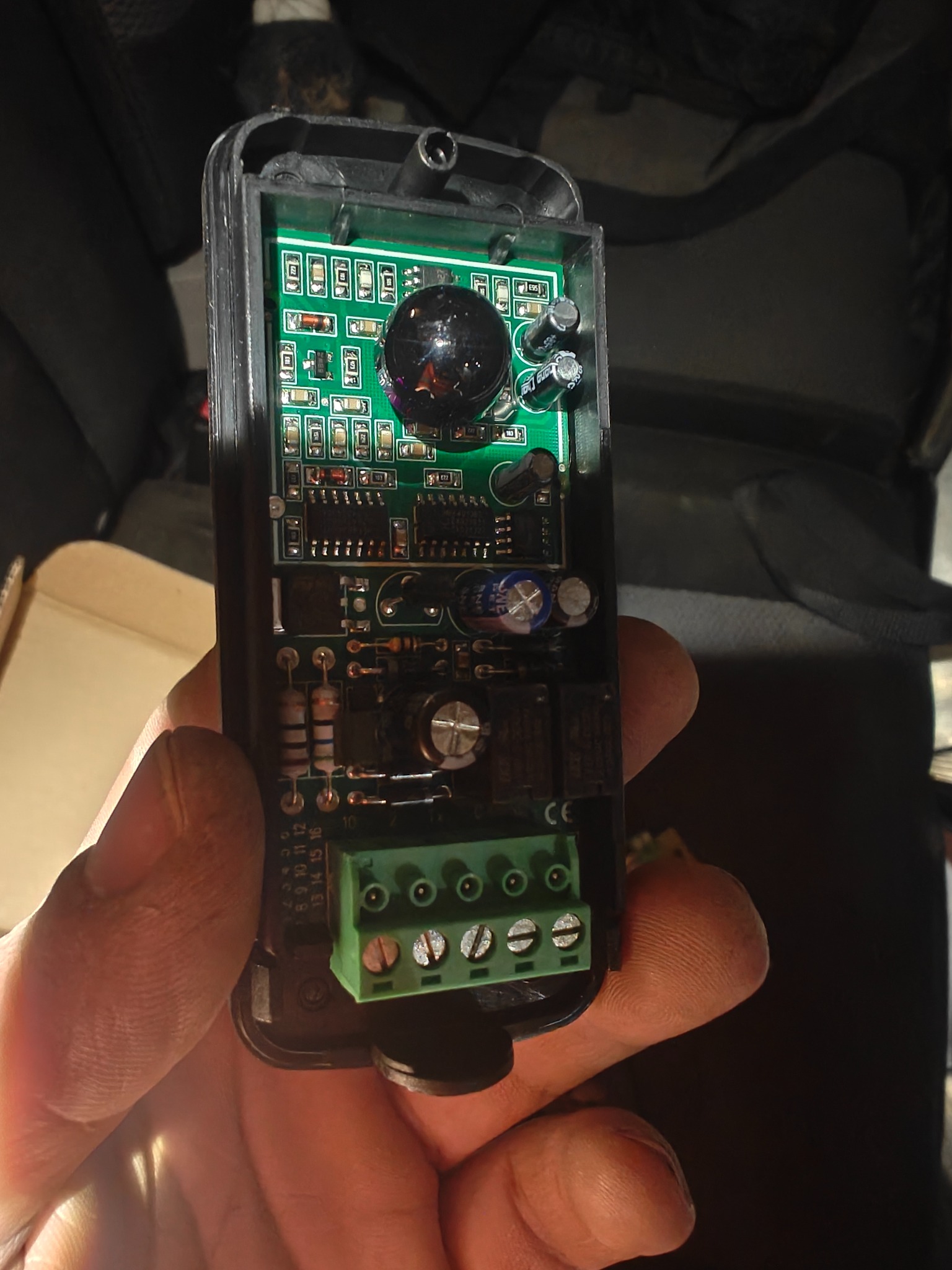 Otwarty pilot do bramy z widoczną elektroniką, zieloną płytką drukowaną i złączami śrubowymi, trzymany w dłoni. Widoczne elementy elektroniczne.
