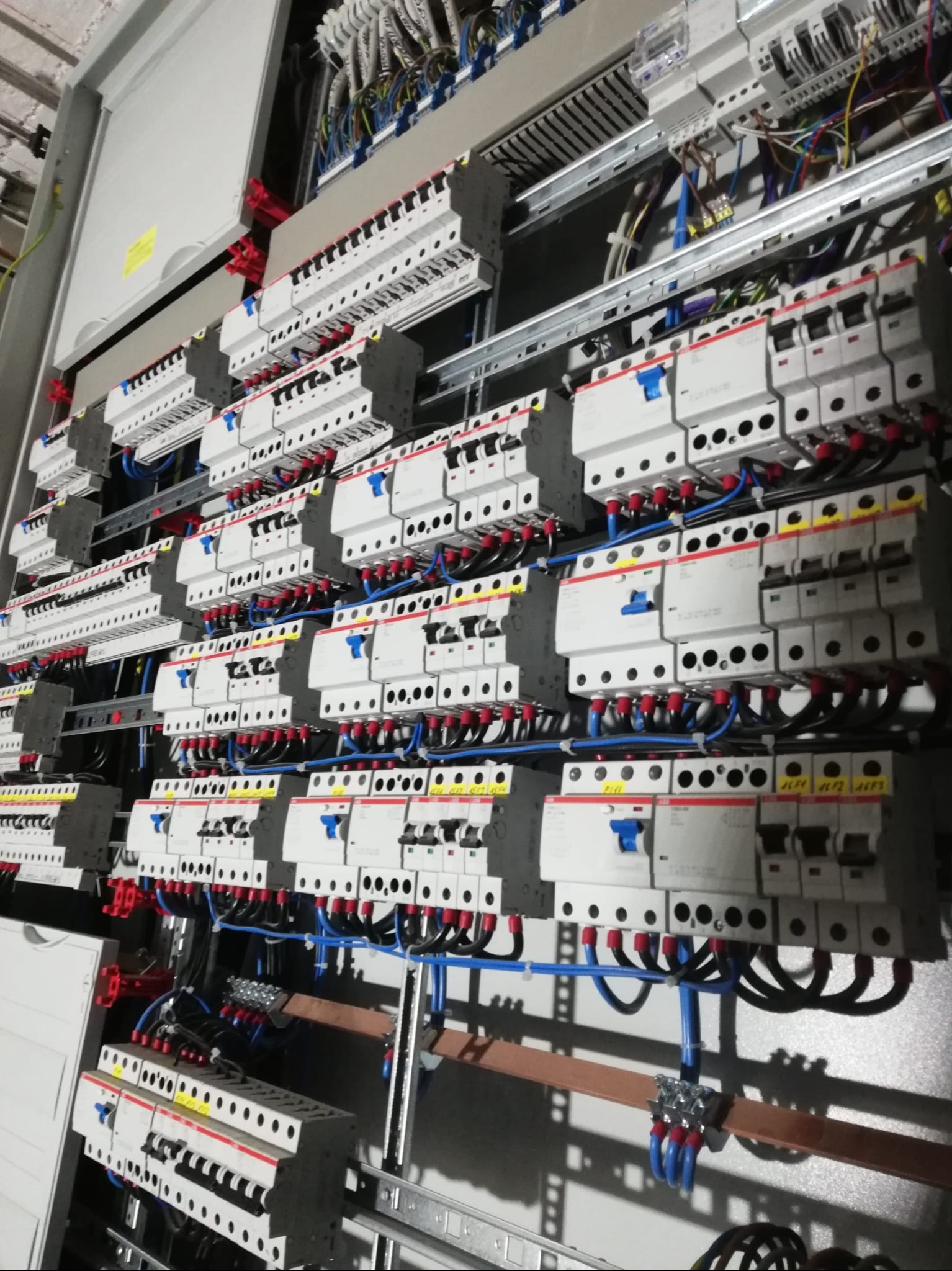 Rozbudowana rozdzielnica elektryczna z licznymi zabezpieczeniami, przewodami i szynami, ukazująca skomplikowaną instalację elektryczną w obiekcie przemysłowym.