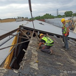 KRB POLSKA SPÓŁKA Z OGRANICZONĄ ODPOWIEDZIALNOŚCIĄ - Demontaż dachu przez dwóch pracowników w kaskach i kamizelkach w Katowicach. Widoczny fragment konstrukcji i łańcuch. Prace rozbiórkowe w toku, pochmurne niebo.