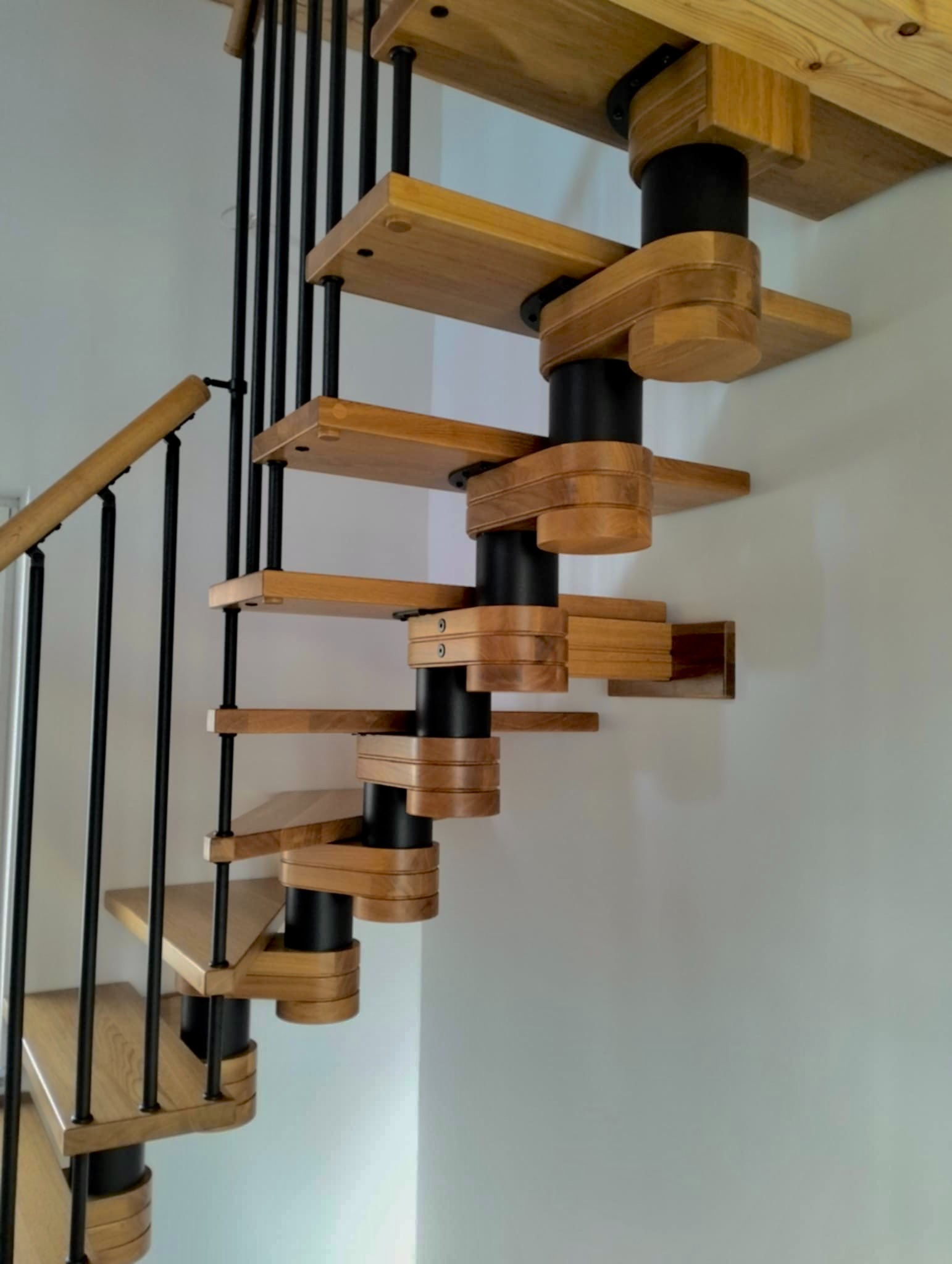 Spiralne schody drewniane z czarną metalową konstrukcją, widok z dołu, oświetlenie naturalne, minimalistyczny design.