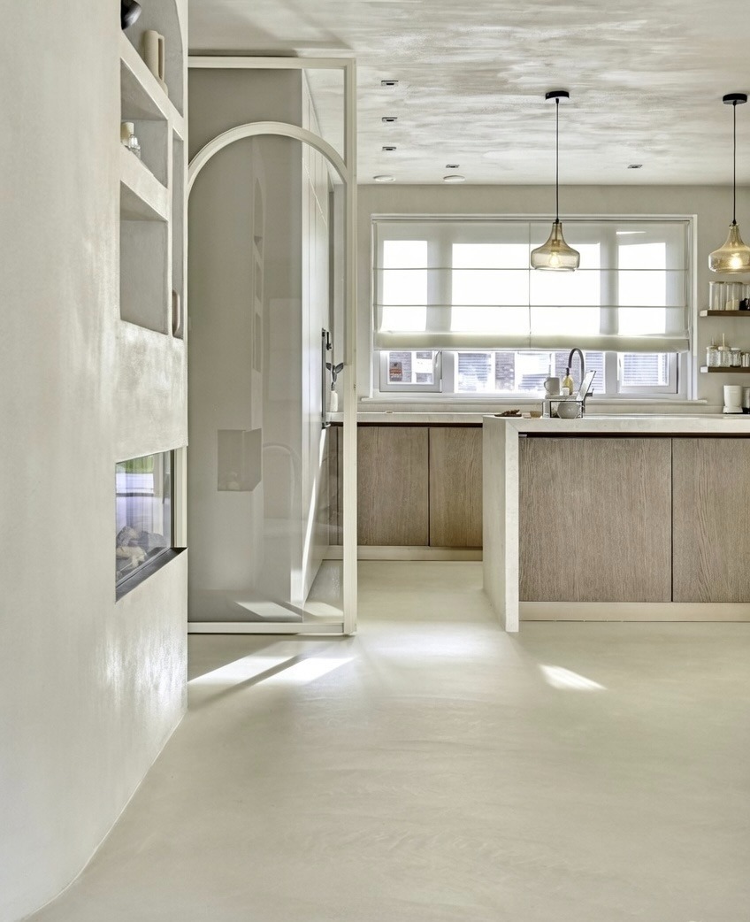 Jasna, minimalistyczna łazienka z kabiną prysznicową w stylu loft, wykończona mikrocementem na ścianach i podłodze. Widoczne oświetlenie i elementy dekoracyjne.