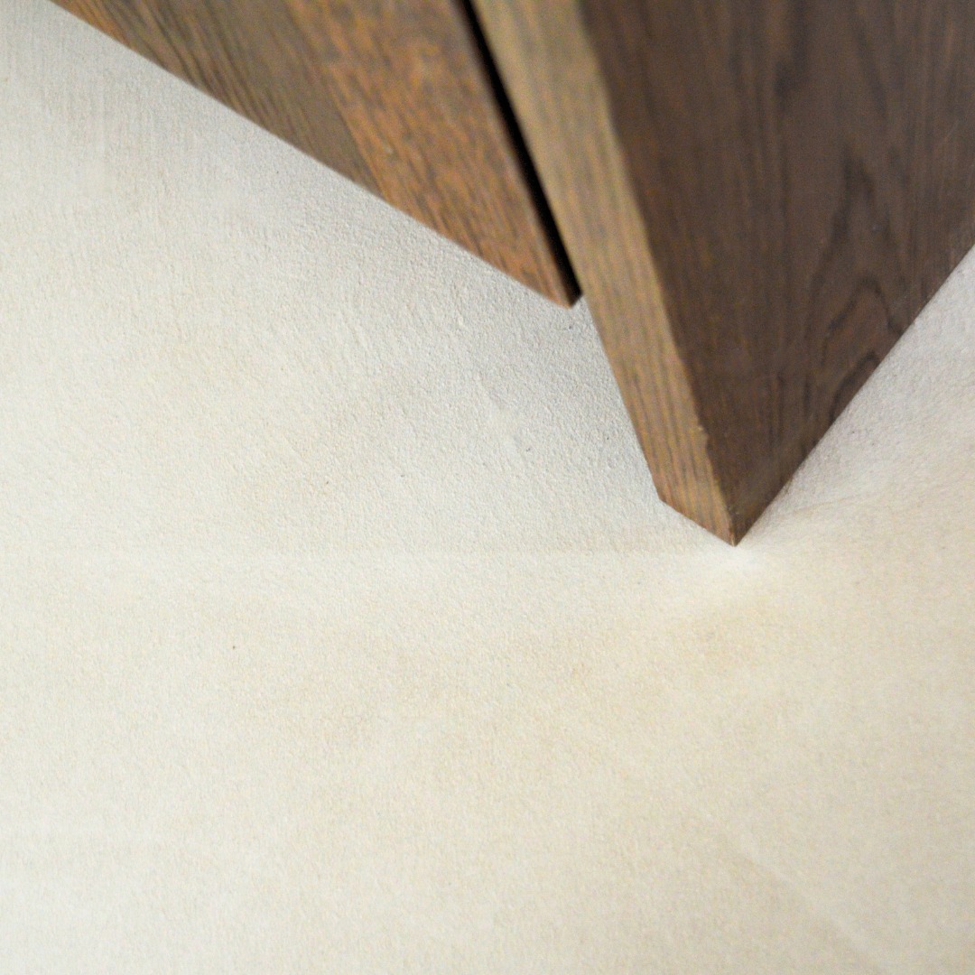 Fragment drewnianej szafki łazienkowej z bliska, z delikatną fakturą ściany w tle. Ujęcie z dołu, podkreślające minimalistyczny design i naturalne materiały.