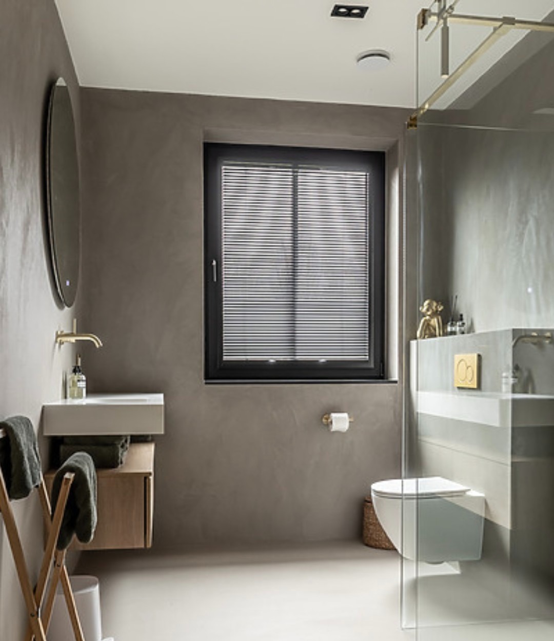 Nowoczesna łazienka z wykończeniem ścian w odcieniach szarości, minimalistyczną umywalką i kabiną prysznicową ze złotymi detalami. Okno z żaluzjami.