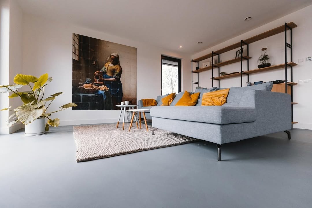 Szara, gładka posadzka w nowoczesnym salonie z szarą sofą, dywanem i obrazem na ścianie. Minimalistyczne wnętrze z rośliną w doniczce.
