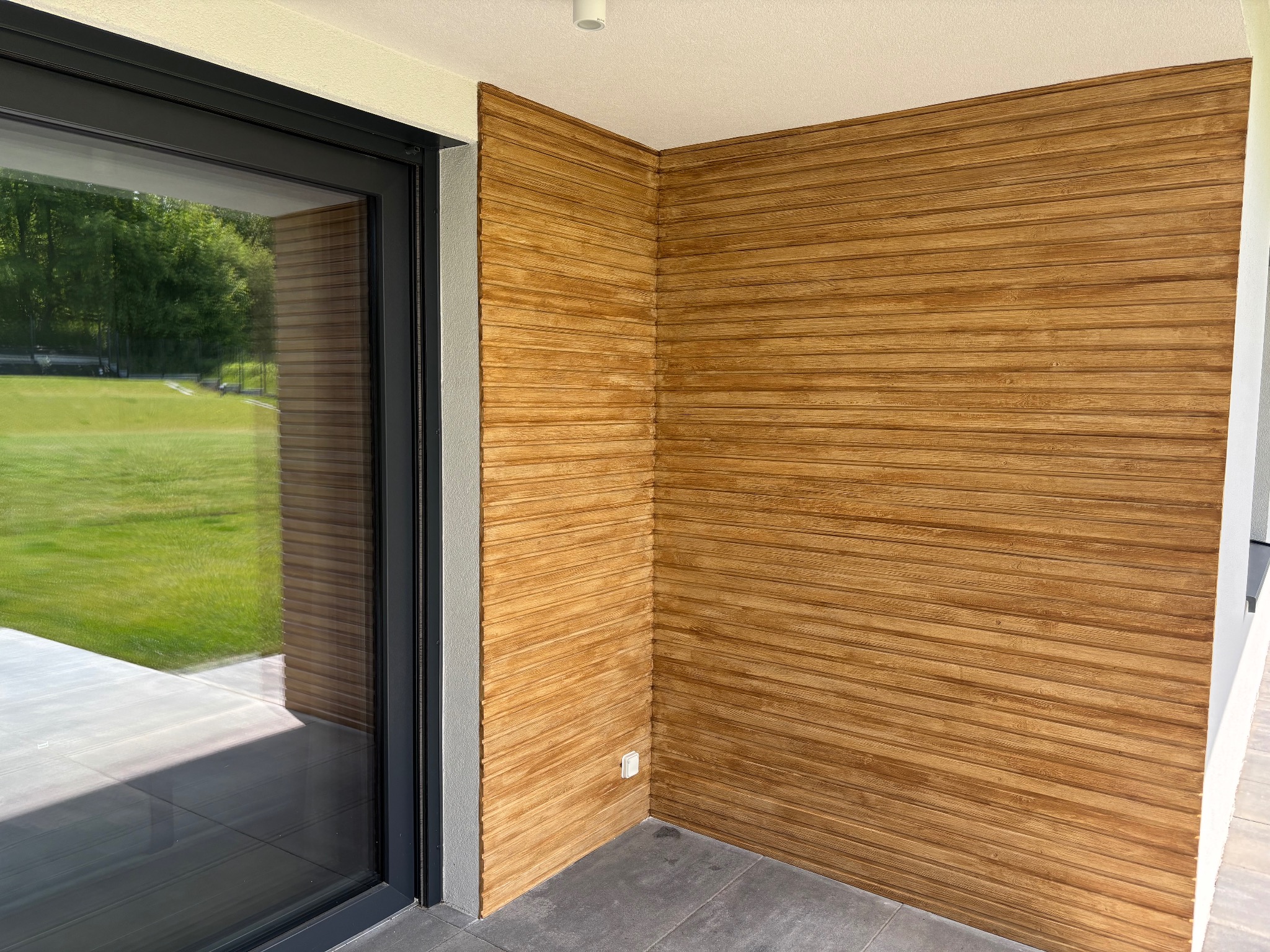 Drewniana okładzina ścienna w Tarnowskich Górach, z widocznym fragmentem okna i szarą podłogą. Dekoracyjne wykończenie wnętrza z poziomymi panelami.