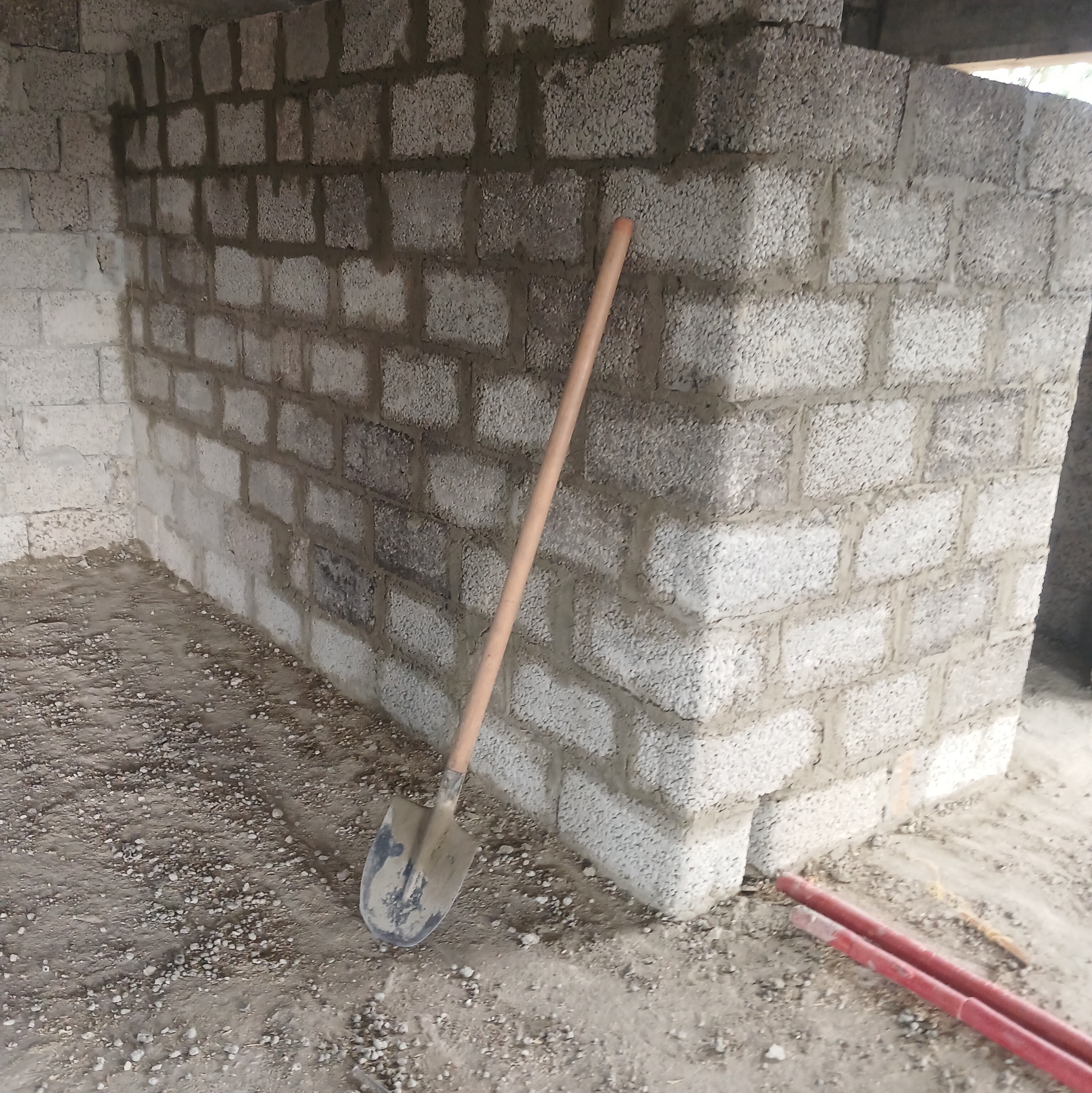 Ściana z betonu komórkowego w trakcie budowy, widoczna zaprawa i narzędzie - łopata oparta o ścianę. W tle widoczne elementy konstrukcyjne budynku.