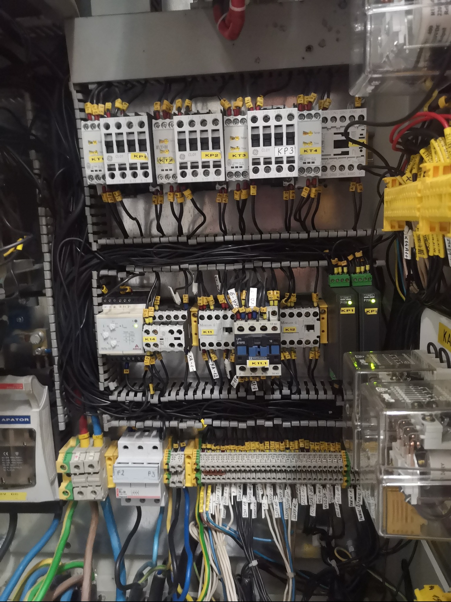 Rozbudowana szafa sterownicza z licznymi przekaźnikami, bezpiecznikami i okablowaniem, ukazująca złożoność systemu elektrycznego w szarej obudowie.