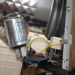 Burklin Marcin Burak - Wnętrze zmywarki w Toruniu z widocznym kondensatorem i elementami elektrycznymi. Detal naprawy AGD, widoczne narzędzia w tle. Nietypowe ujęcie z góry.