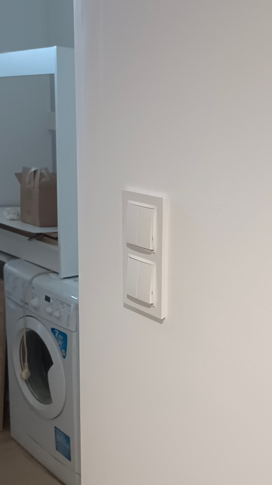 Biały podwójny włącznik światła na świeżo pomalowanej ścianie w łazience, obok pralki. Minimalistyczny design.