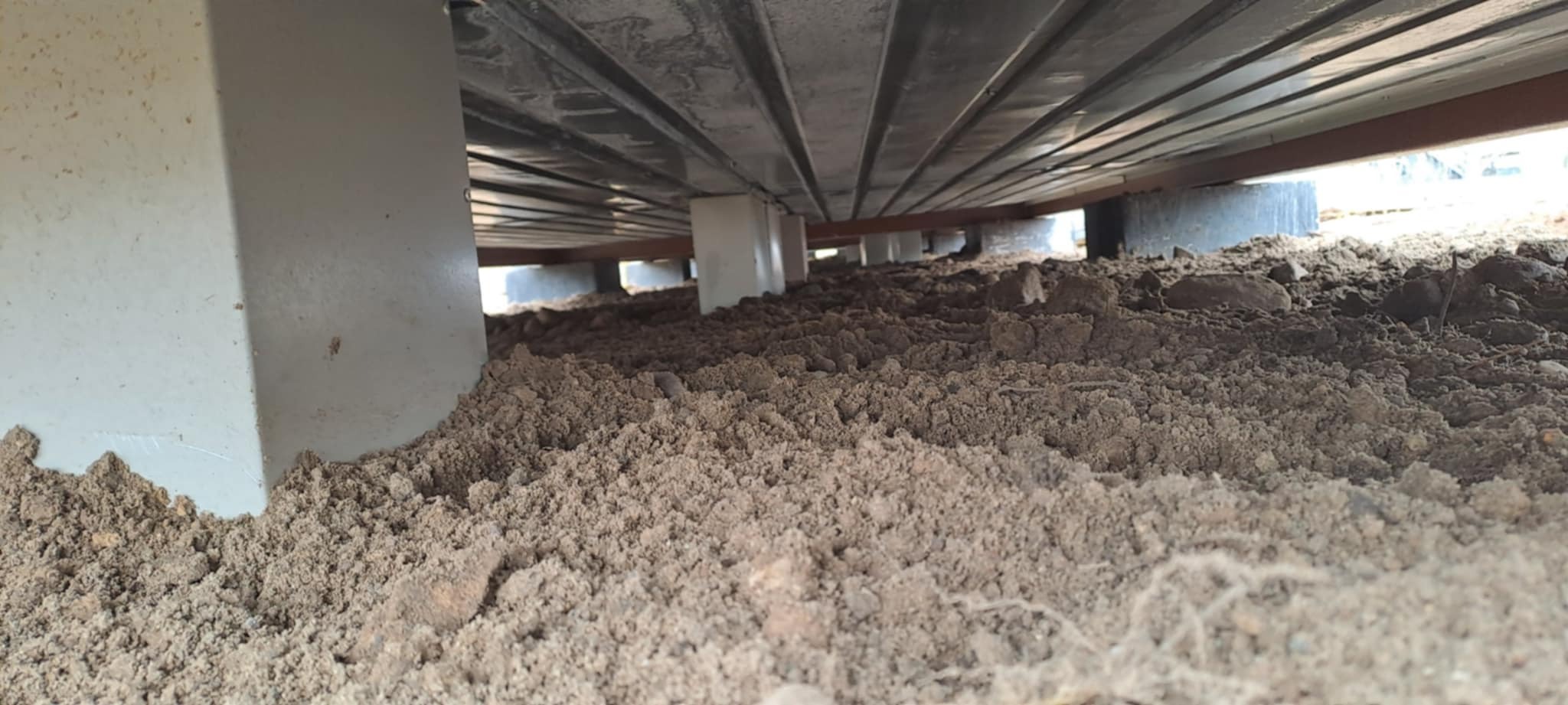 Nietypowy widok spod konstrukcji: metalowe belki i podpory na ziemi, perspektywa żaby, ukazująca fundamenty budynku w trakcie prac ziemnych.