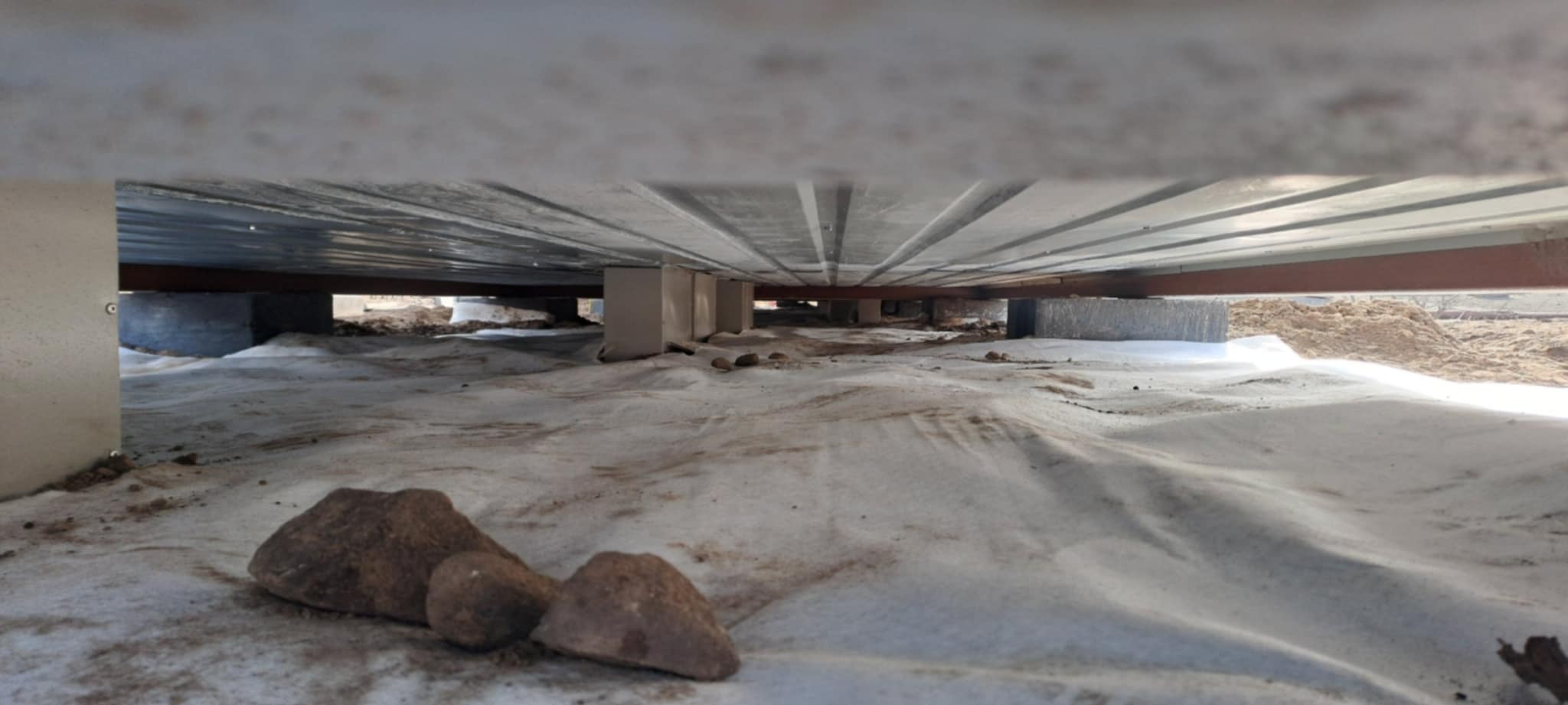 Widok z dołu na konstrukcję pod podłogą, z widoczną izolacją i elementami wsporczymi. Ujęcie z perspektywy ziemi, podkreślające detale konstrukcyjne.