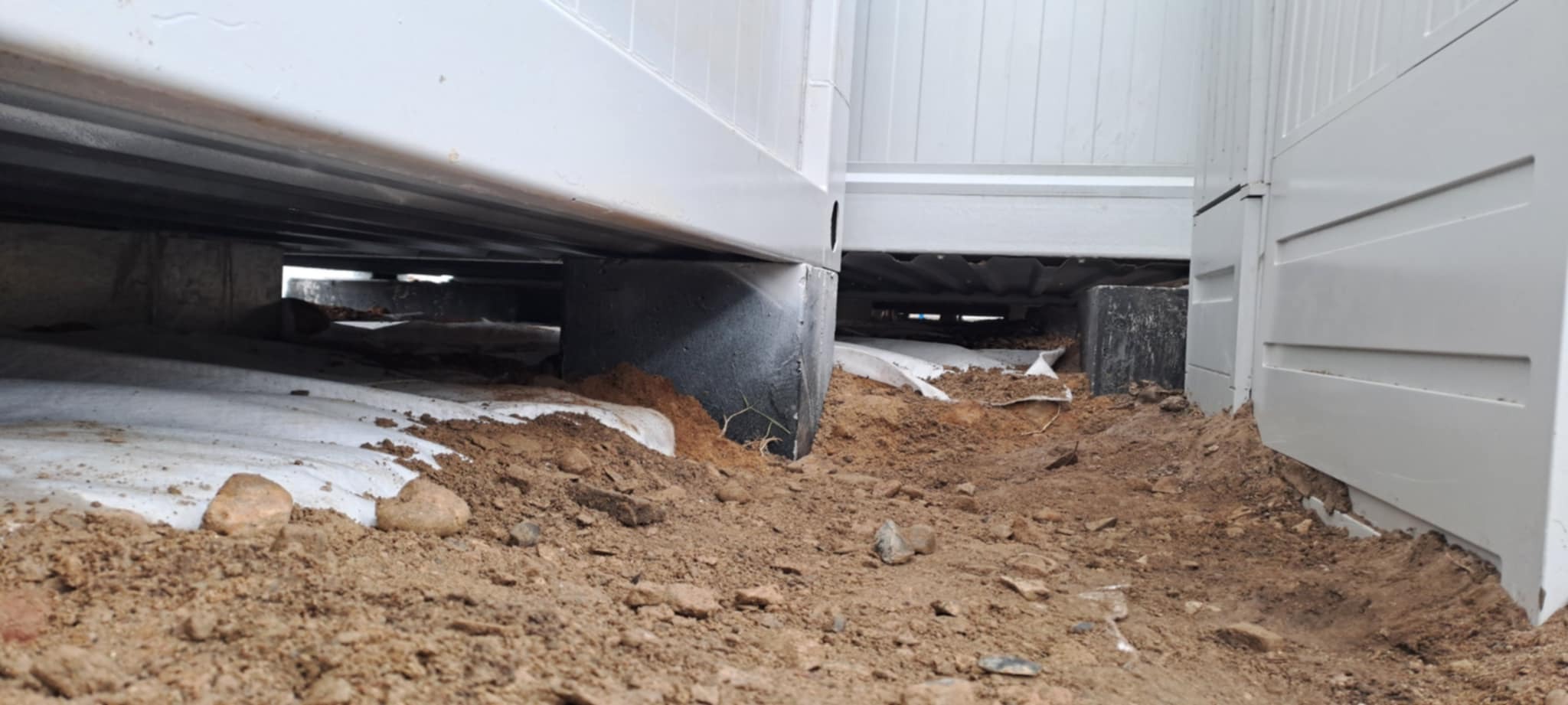 Fundamenty pod kontenery biurowe na gruncie, zabezpieczone geowłókniną. Widoczne betonowe bloki i ziemia. Ujęcie z dołu, podkreślające konstrukcję.