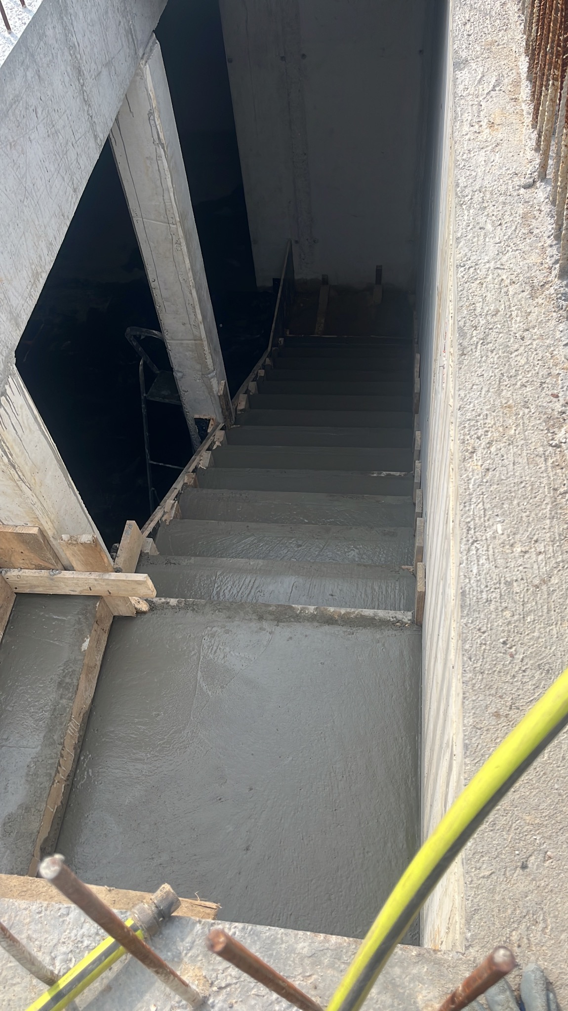 Wylane betonowe schody w surowym stanie, widoczne drewniane szalunki i zbrojenia. Ujęcie z góry, ukazujące detale konstrukcji i fakturę betonu.